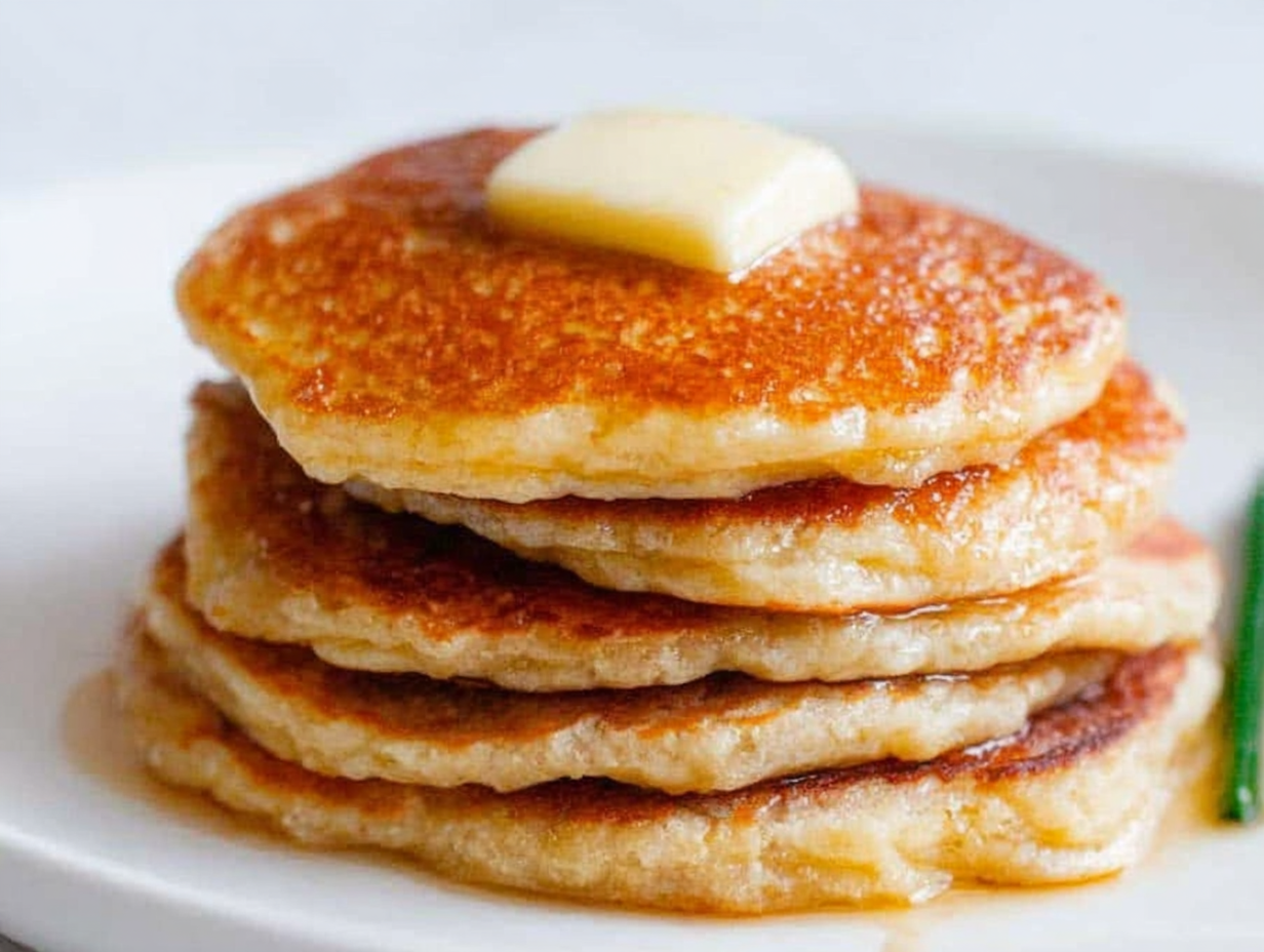 A stack of healthy oatmeal apple pancakes topped with fresh apple slices and a drizzle of maple syrup.